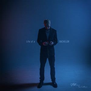 Person in a dark suit standing against a blue background with text 'Life of a Bachelor' displayed.