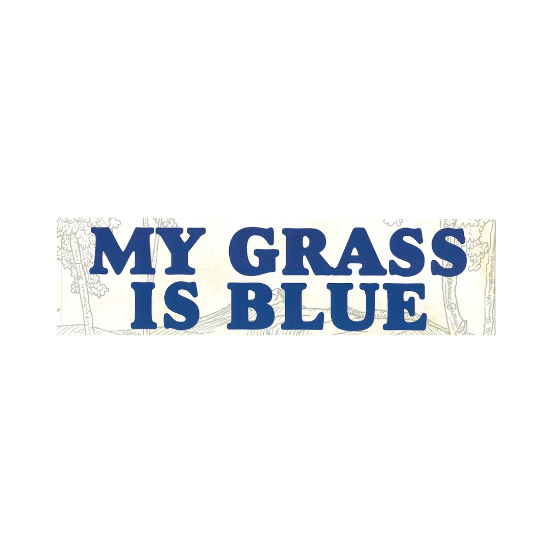 A rectangular bumper sticker or sign with the phrase 'MY GRASS IS BLUE' in large blue block letters over a cream background with faint line-drawn trees and grass.