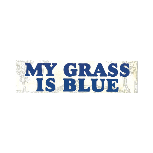 A rectangular bumper sticker or sign with the phrase 'MY GRASS IS BLUE' in large blue block letters over a cream background with faint line-drawn trees and grass.